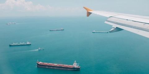 View from an airplane window of bulk cargo ships scattered across turquoise sea below the wing