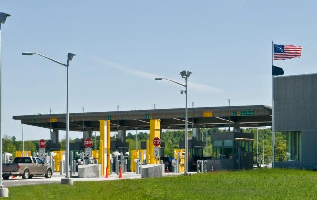 U.S. border crossing checkpoint with numbered inspection lanes, stop signs, and an American flag flying beside the station