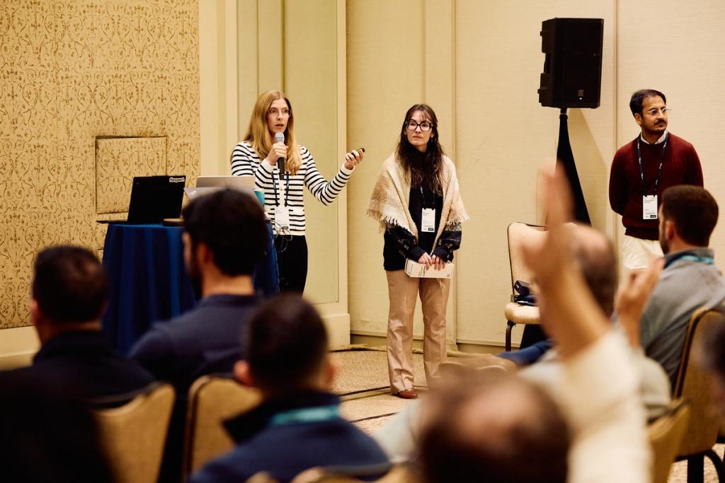 Two women presenting with a microphone and clicker to a seated audience at a conference session