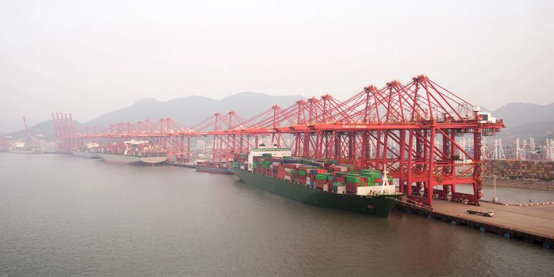 Container ship berthed at the Port of Ningbo with a long line of red gantry cranes in haze