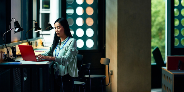 Woman working on a laptop at a desk in a dimly lit modern office, evoking data-driven trade decisions.