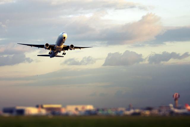 White passenger jet climbing into a cloudy dusk sky just after takeoff above an airport