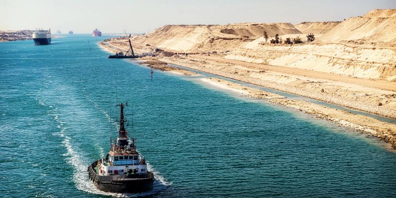 Tugboat navigates the Suez Canal with cargo ships and sandy desert banks ahead