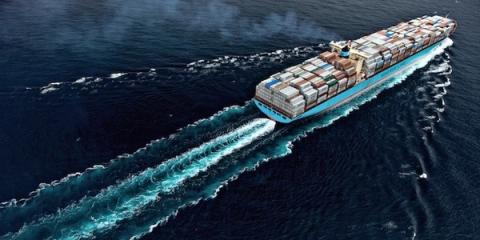 Aerial view of a Maersk container ship loaded with cargo cutting a foamy wake across dark open ocean