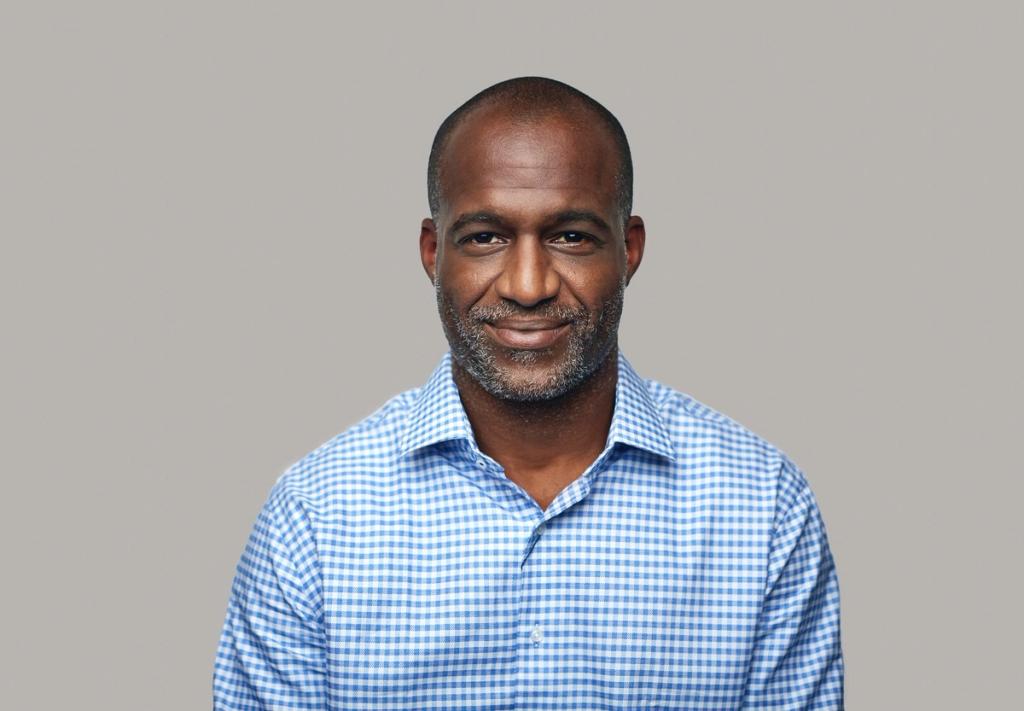 Portrait of a man smiling at the camera wearing a blue checkered shirt.