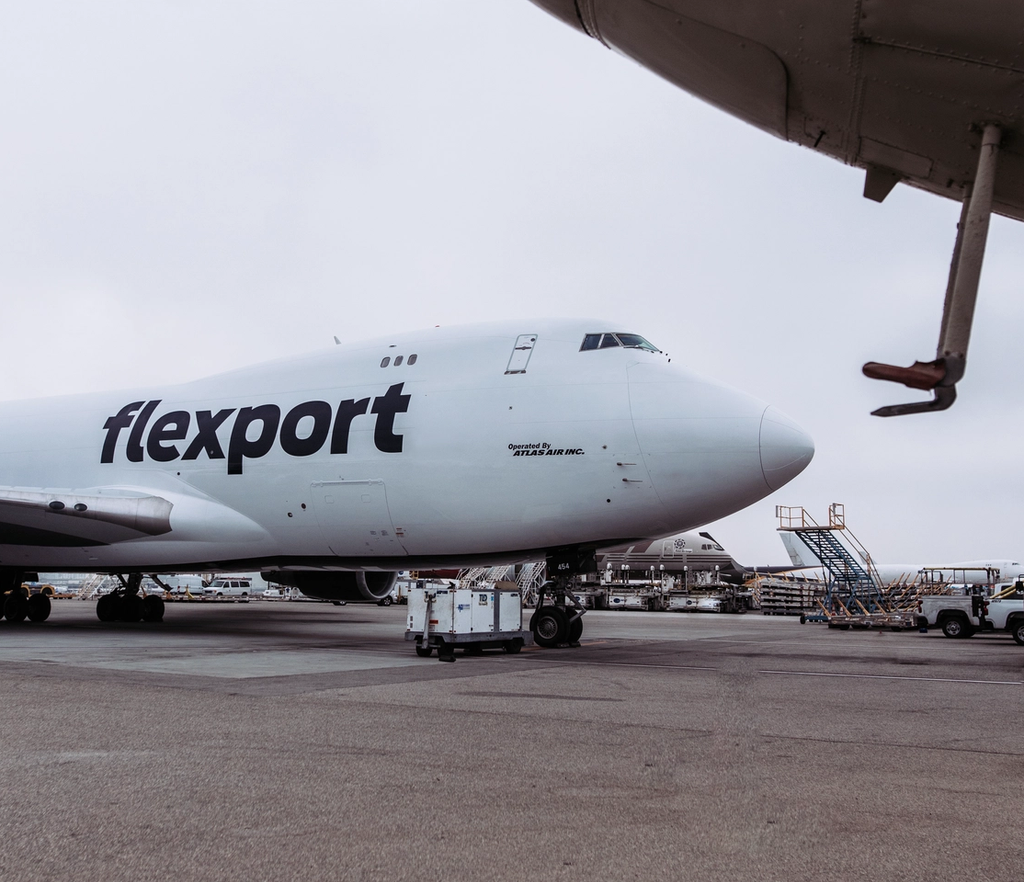 Flexport cargo aircraft parked at airport with ground support equipment nearby.