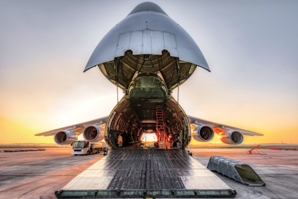 Large cargo aircraft with open cargo door and loading ramp extended on runway.