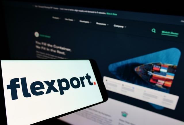Smartphone showing the Flexport wordmark logo in front of a blurred screen of the Flexport website