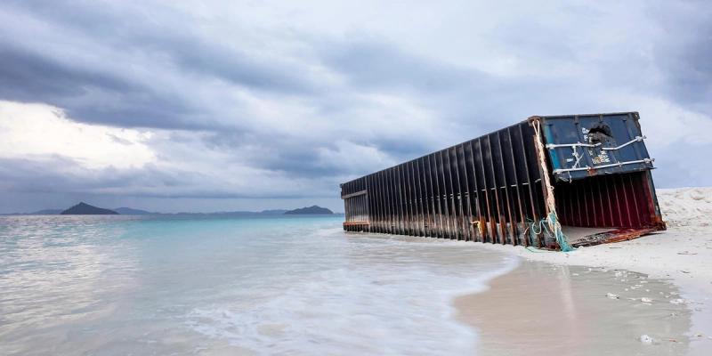 Lost shipping container washed up on a white sand beach under a cloudy sky