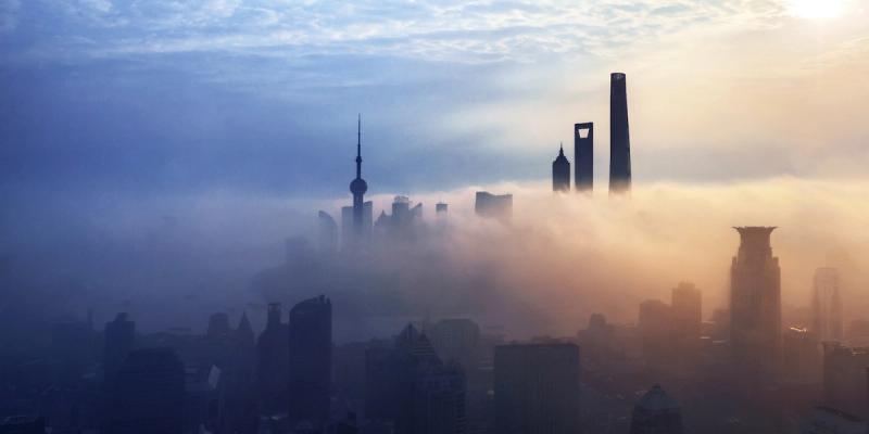 Shanghai skyline with the Oriental Pearl Tower and skyscrapers shrouded in fog at sunrise.