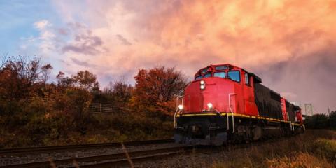 Red freight locomotive on tracks at sunset beside autumn trees