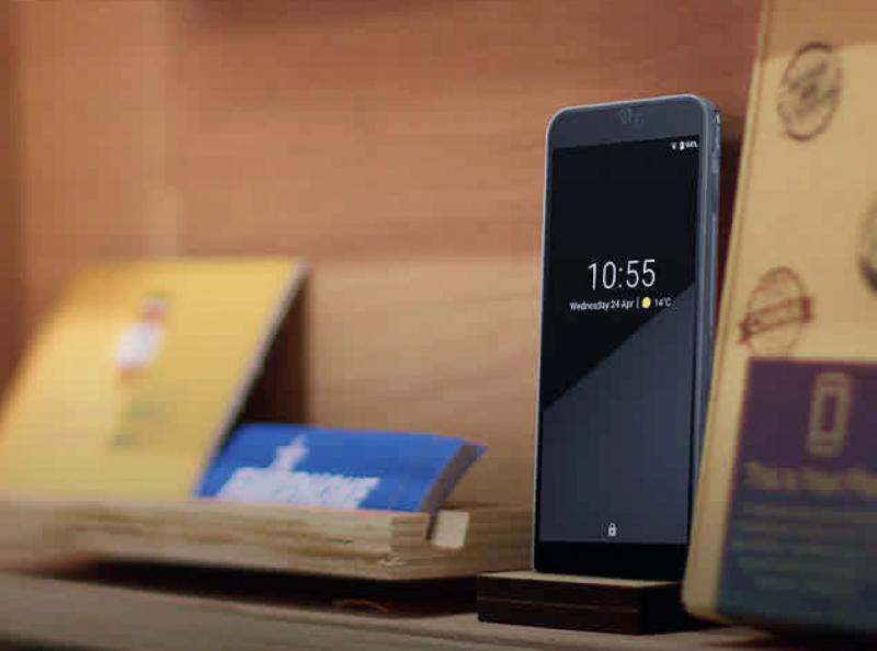 Fairphone smartphone standing upright beside its cardboard packaging on a wooden shelf