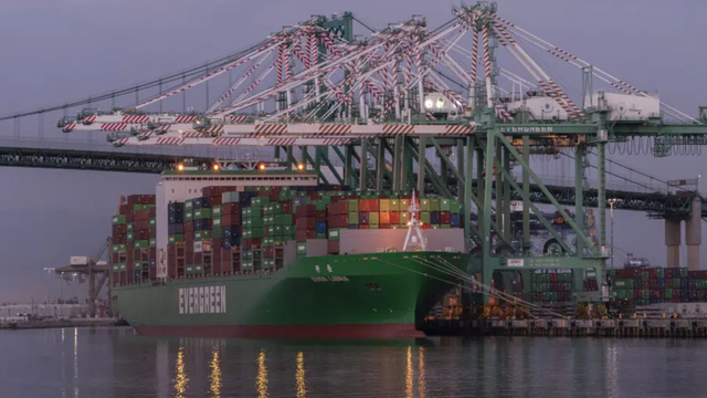 Container ship loaded with cargo docked at a port terminal beneath gantry cranes at dusk
