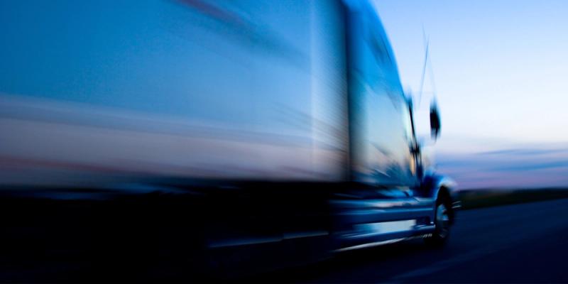 Motion-blurred semi truck speeding along a highway at dusk