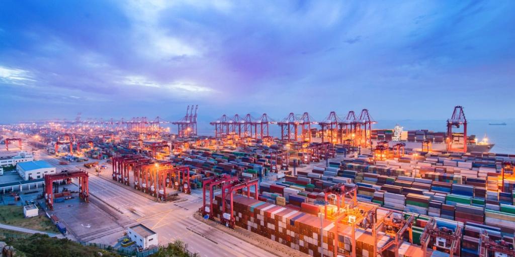 Aerial dusk view of a busy container port with stacked containers and gantry cranes lit orange