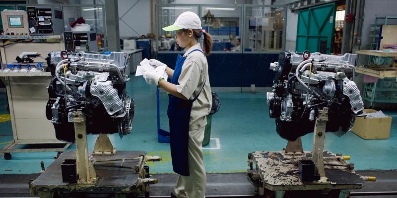 Worker in cap and gloves inspecting paper between two engines on a factory assembly line