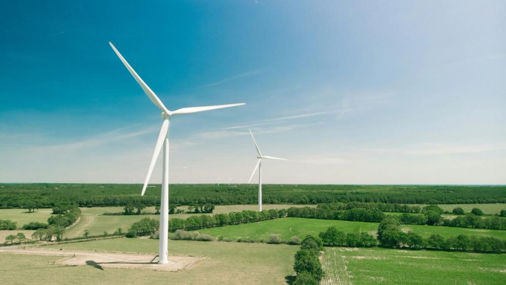 Two wind turbines on green farmland under a clear blue sky