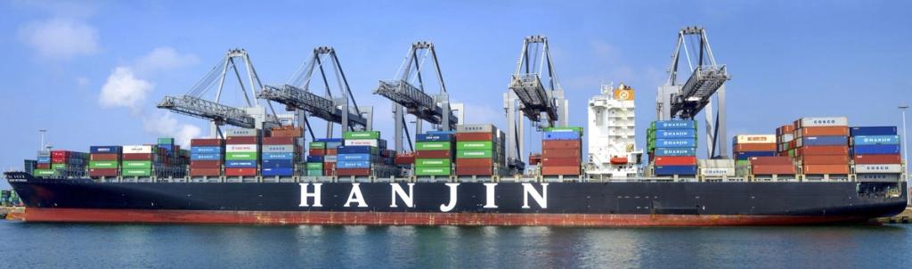 Container ship marked HANJIN docked under gantry cranes, loaded with stacked shipping containers