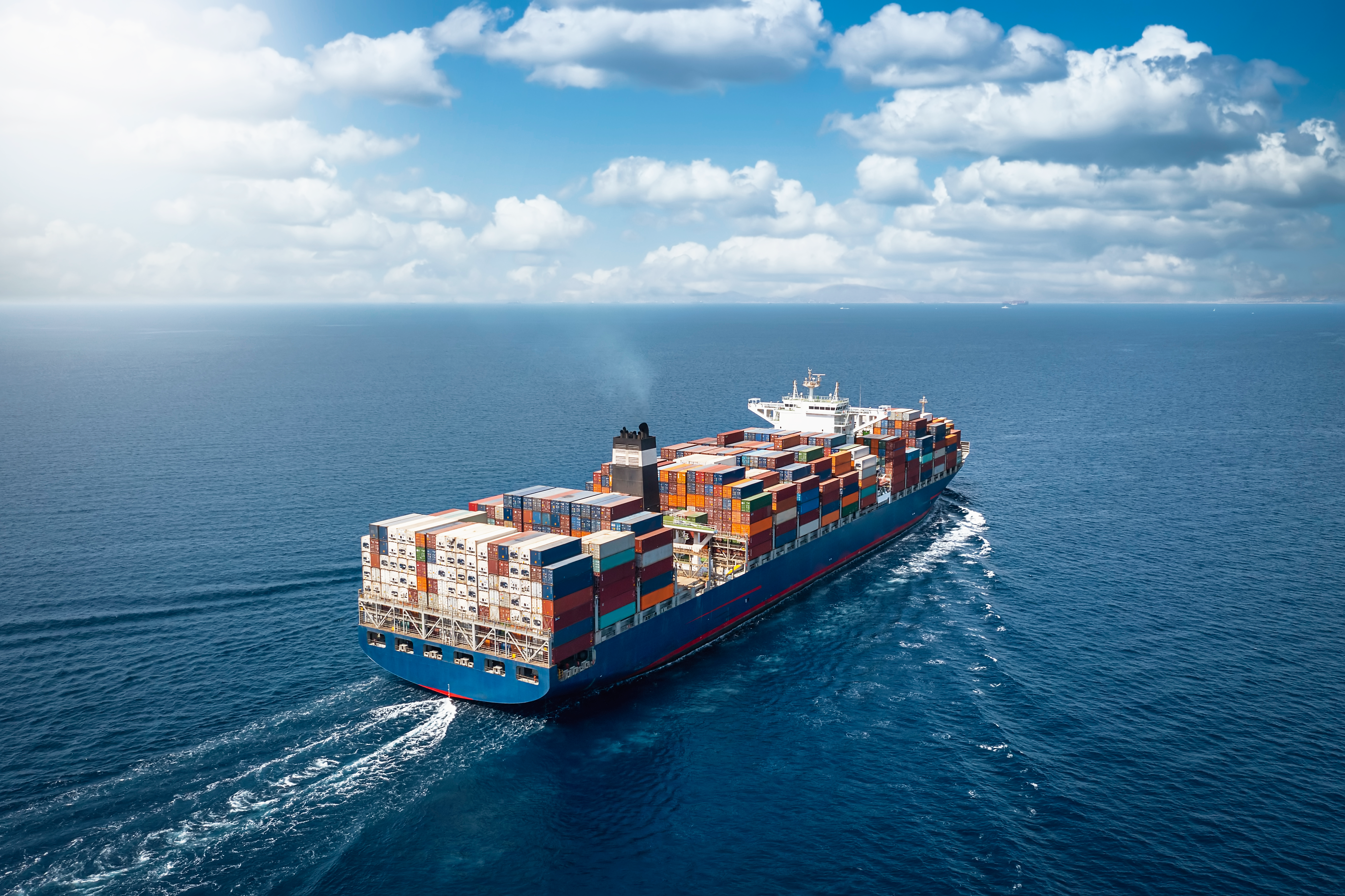 Large cargo ship transporting stacked shipping containers across the open ocean.