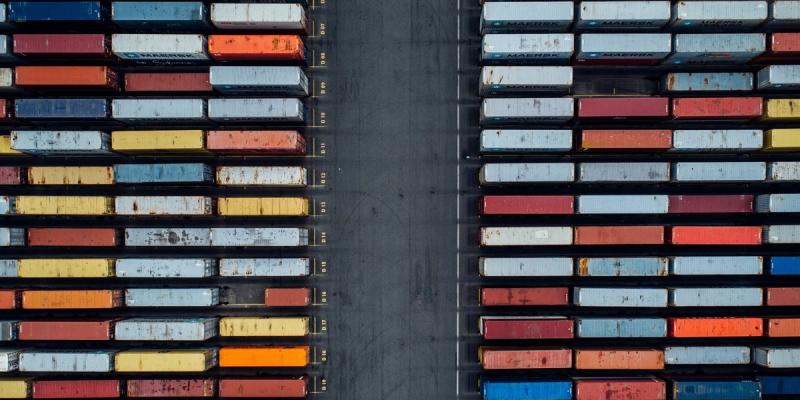 Aerial top-down view of two rows of colorful stacked shipping containers split by a central lane.