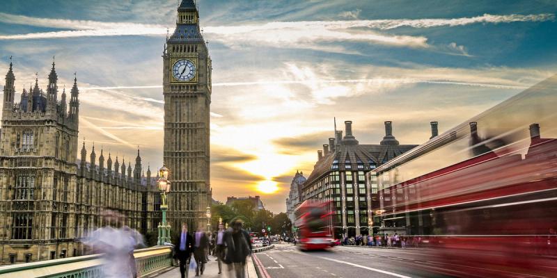 Big Ben and the Houses of Parliament at sunset with red double-decker buses crossing Westminster Bridge
