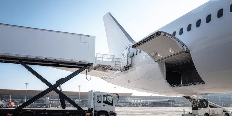 White cargo aircraft at airport with rear loading door open and scissor-lift loader alongside