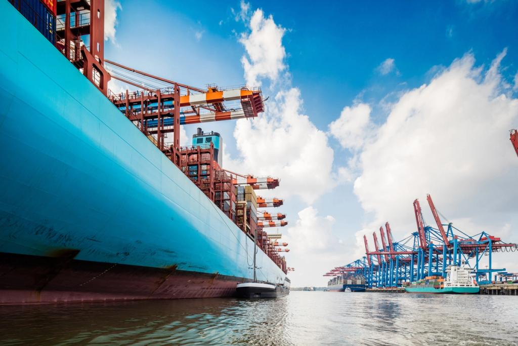 Container ship hull at berth beside red gantry cranes at a terminal under a bright blue sky with clouds