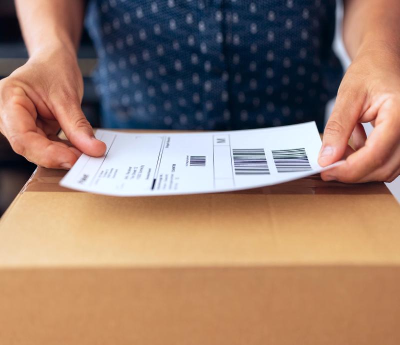 Person applying a printed shipping label to a cardboard box