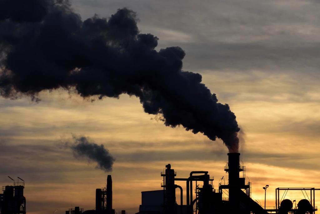 Industrial factory smokestack emitting thick black smoke against an orange sunset sky