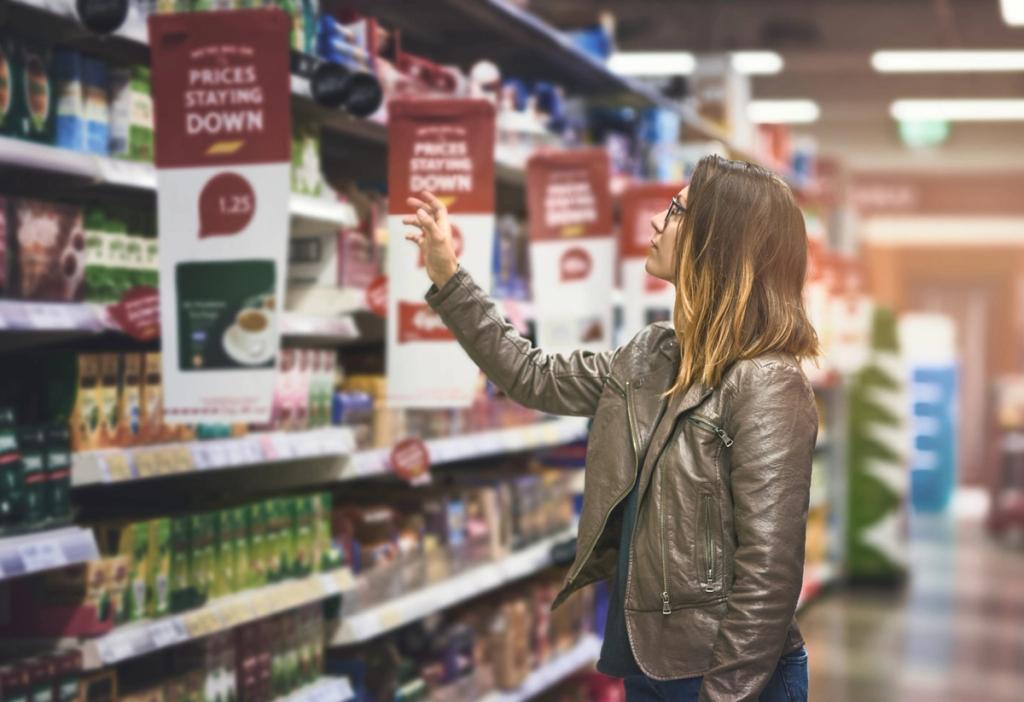 Woman in a leather jacket reaches for a 'Prices Staying Down' shelf tag in a grocery store aisle.