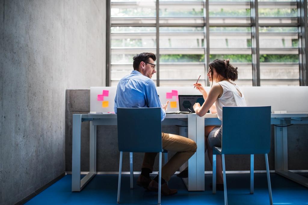 Man and woman seated at a desk reviewing a laptop and sticky notes in a modern office
