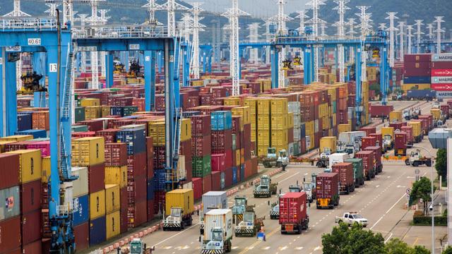 Aerial view of a busy container port with stacked shipping containers, gantry cranes, and trucks hauling containers along loading lanes