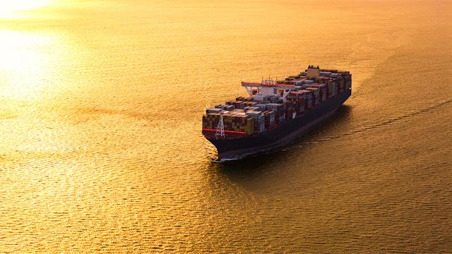 Aerial view of a fully loaded container ship sailing on open water bathed in golden sunset light