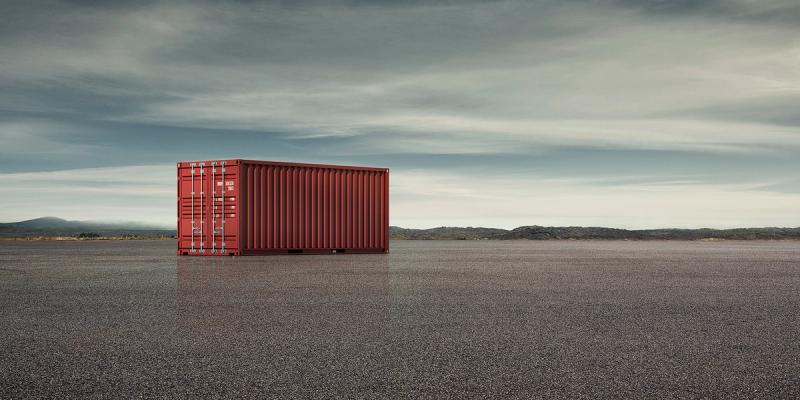 A single red shipping container sitting alone on a vast gravel plain under a cloudy sky