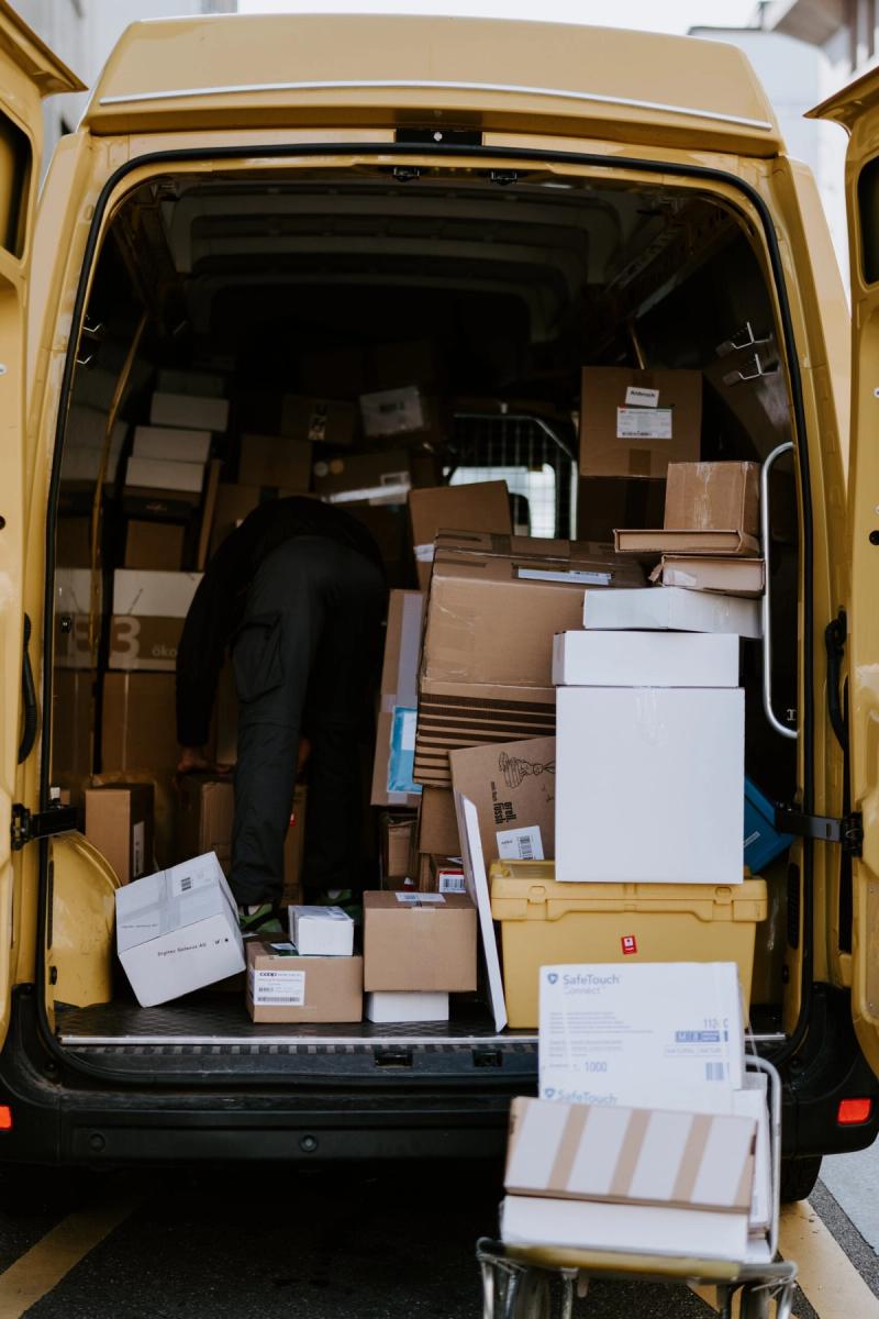 Person loads cardboard boxes and parcels into the open rear of a yellow delivery van