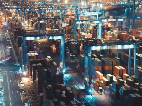 Aerial night view of a container terminal with stacked containers and blue gantry cranes labeled Tianjin Port.
