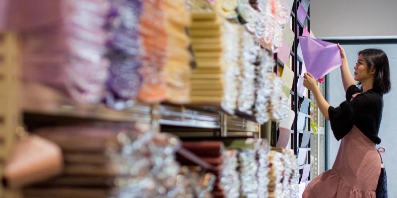 Worker in an apron arranges purple fabric on shelving stocked with rolls of colorful textiles
