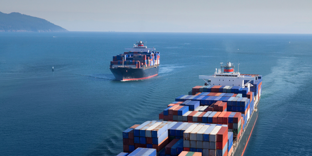 Two container ships passing on the open ocean near a coastline, representing ocean freight shipping