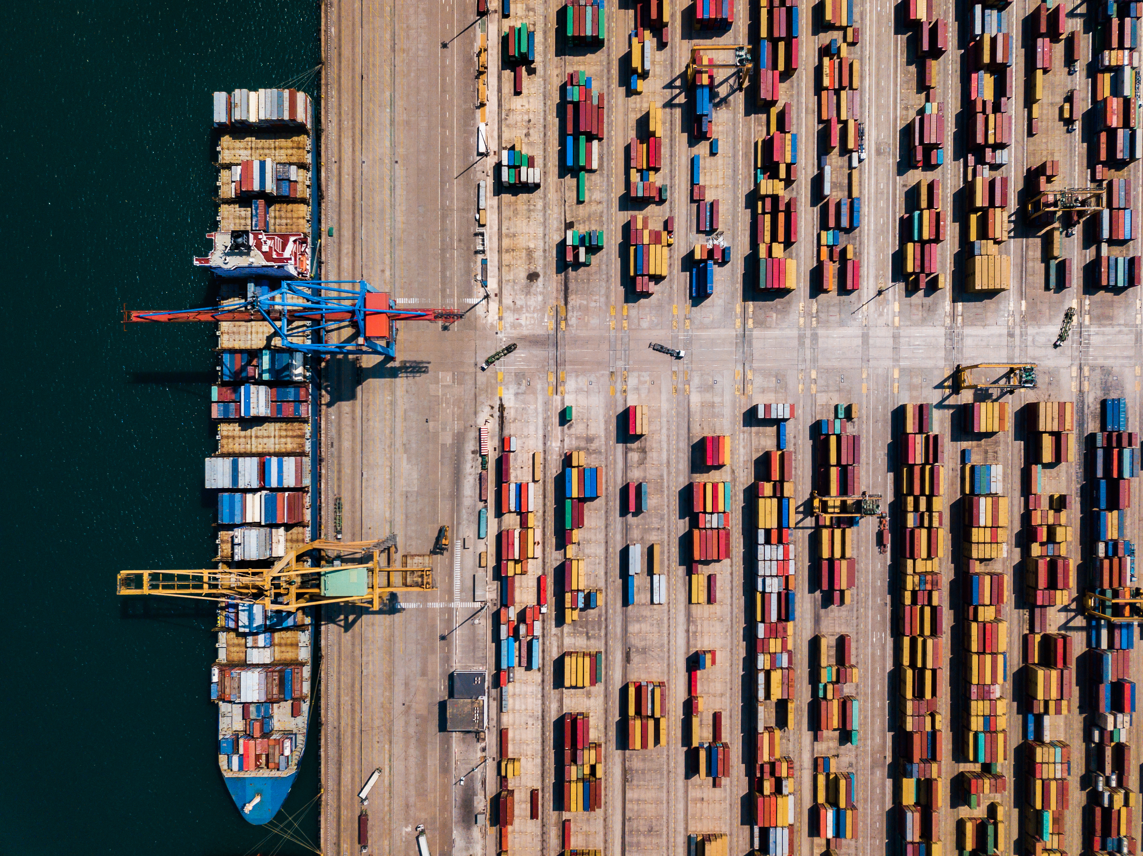 Aerial view of a shipping port with cargo containers being unloaded by container handling equipment.