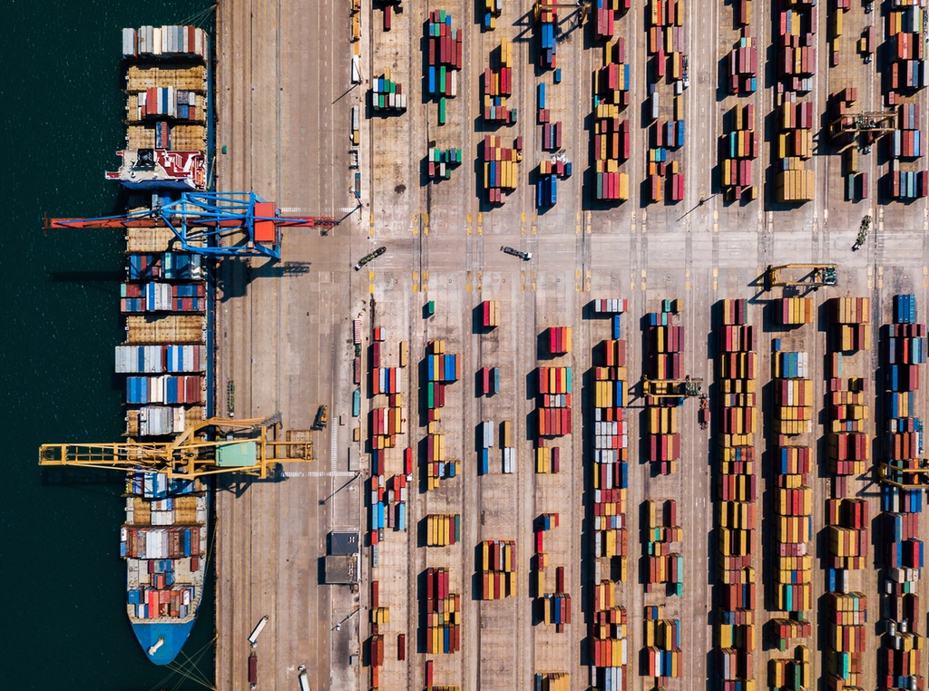 Aerial view of a shipping port with cargo containers being unloaded by container handling equipment.