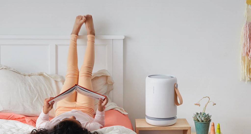 Child lying on a bed reading a book with feet up, white Molekule air purifier on the nightstand