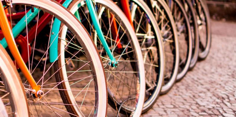 Row of colorful bicycles leaning side by side on a cobblestone street, focused on their wheels and spokes