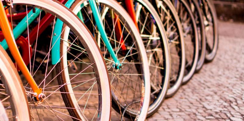 Row of colorful bicycles leaning side by side on a cobblestone street, focused on their wheels and spokes