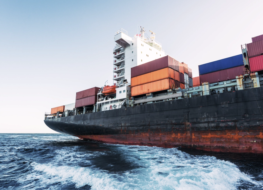A cargo ship loaded with shipping containers travels through ocean waters.