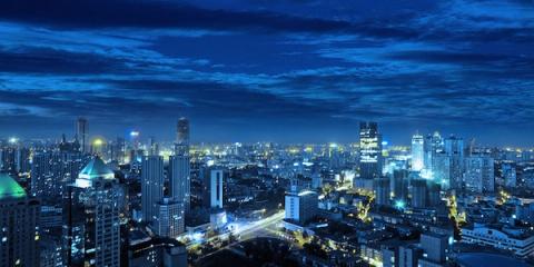 City skyline of lit high-rise towers at blue twilight under a cloudy sky