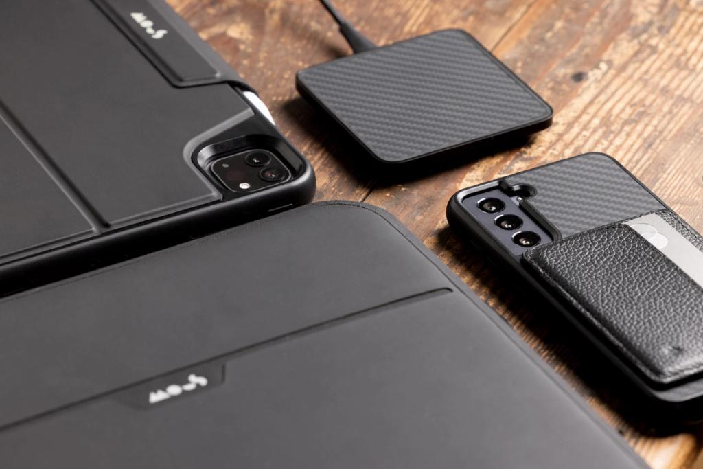 Black Mous phone and tablet cases and a wireless charger arranged on a dark wood surface
