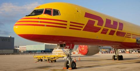 Yellow and red DHL cargo jet parked on an airport tarmac with ground equipment beneath it
