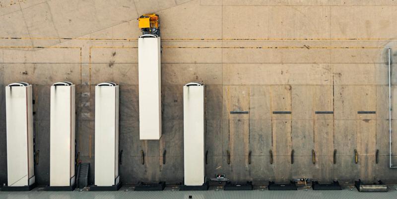 Aerial view of white box trucks and a yellow cab truck backed into loading dock bays at a warehouse