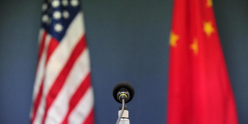 Microphone in foreground with blurred U.S. and Chinese flags flanking it against a blue wall