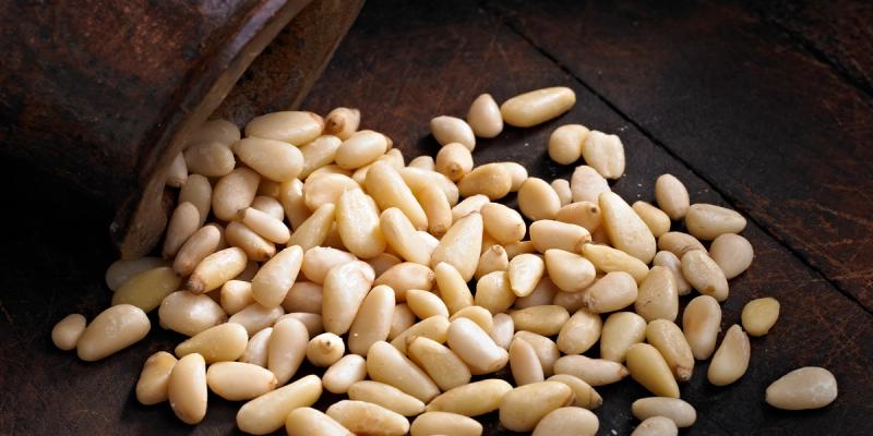 Pine nuts spilling from a rustic metal cup onto a dark wooden surface
